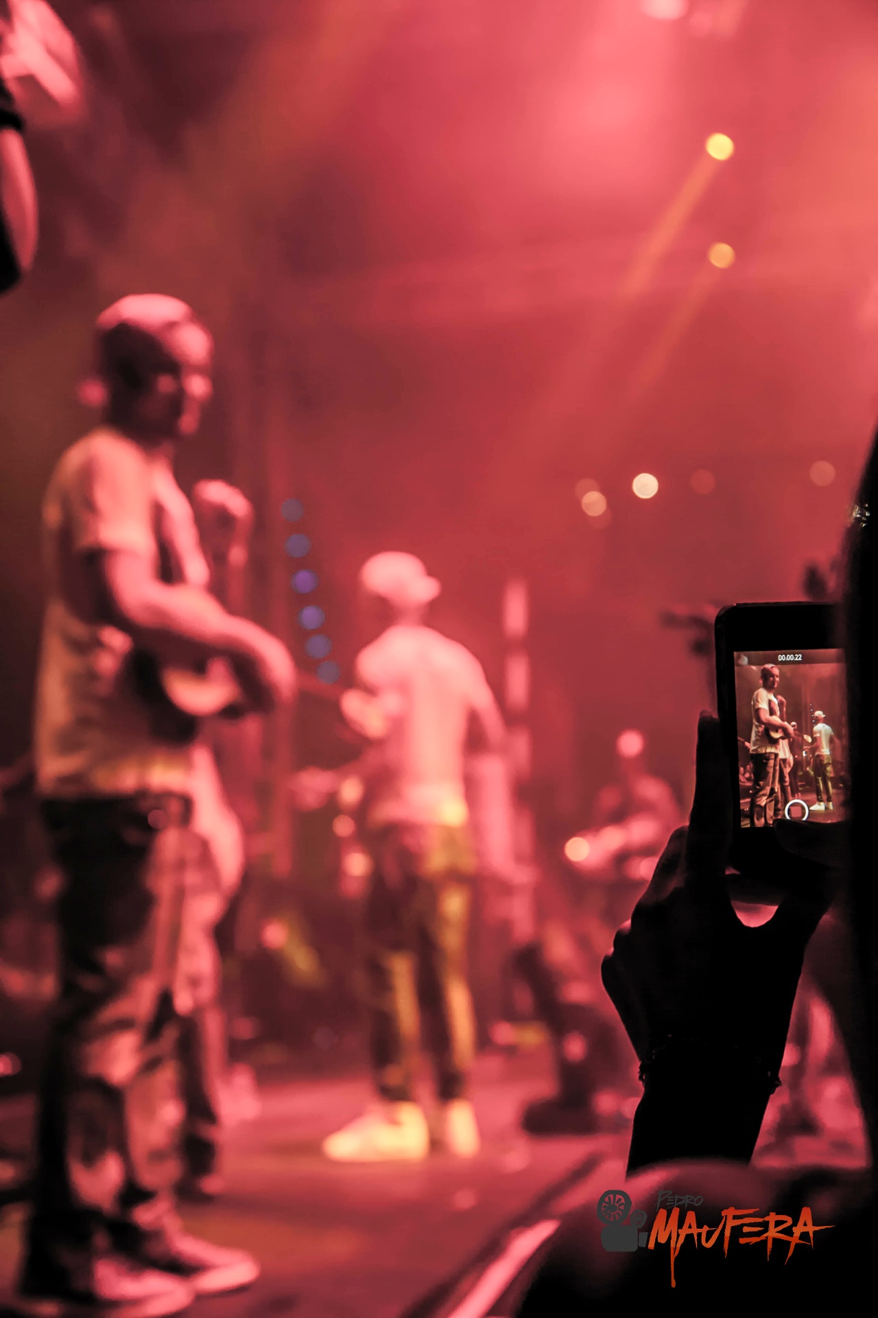 Show em luz vermelha visto pela plateia com celular gravando