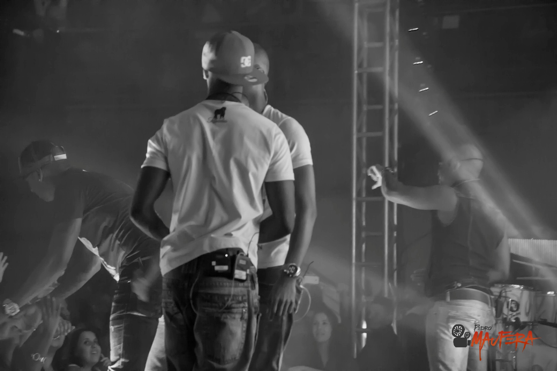 Vocalistas de costas no palco em P&B com fumaça